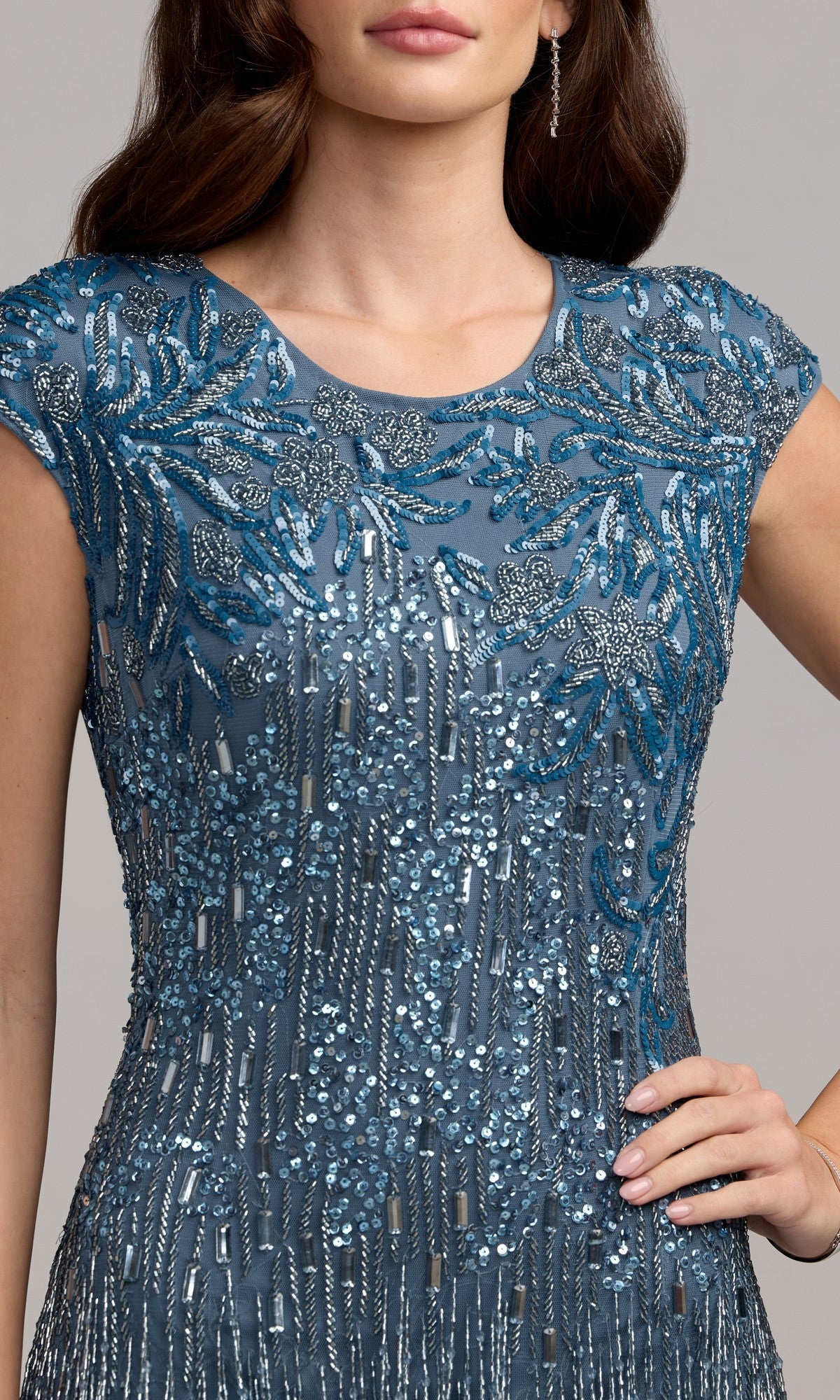Woman in the Beaded Long Lilac Formal Dress, Mac Duggal 6169, embellished with intricate beadwork and sequins, stands with one hand on her hip; her face is partially out of view.